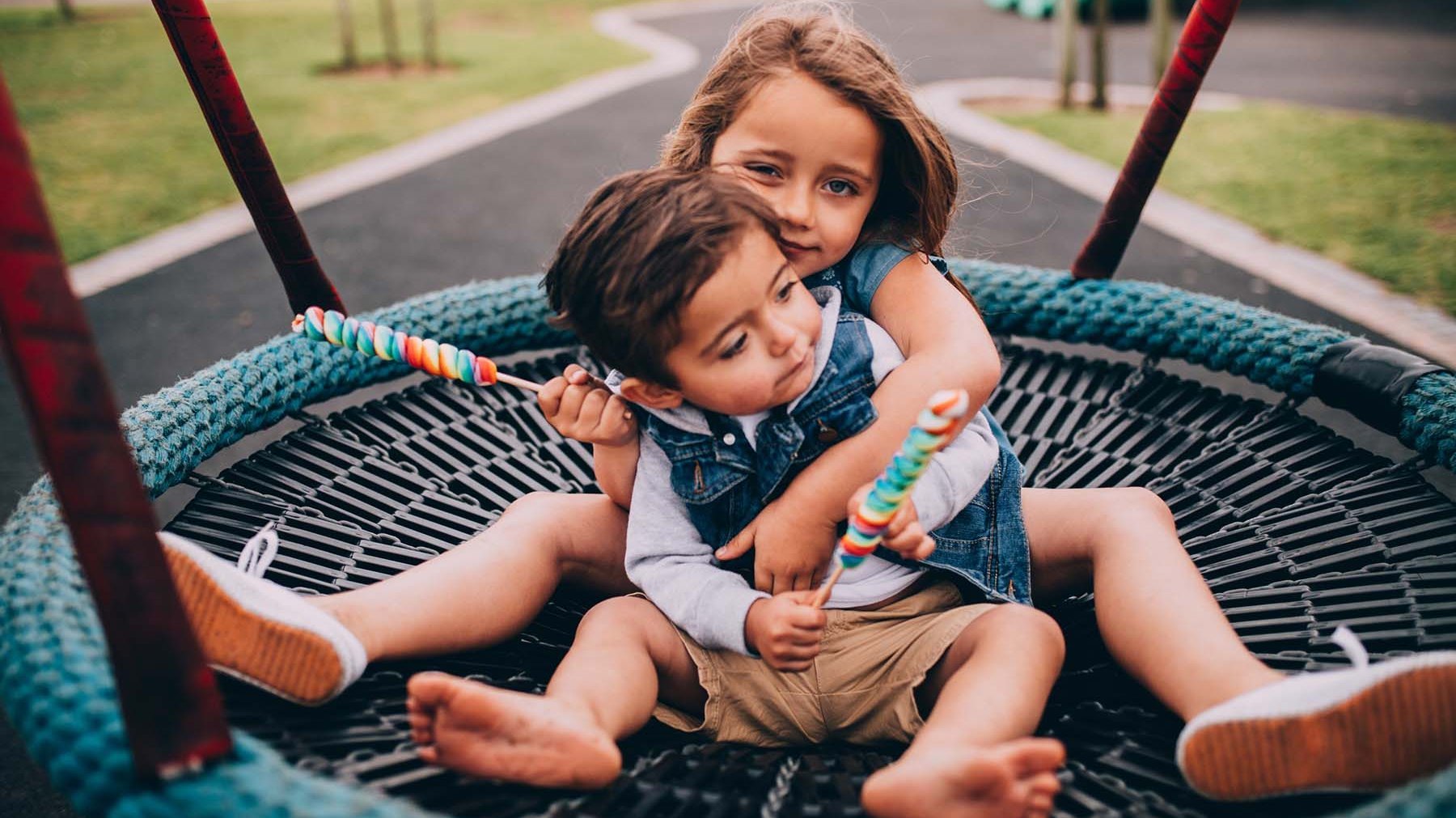 Zwei Kinder sitzen in einer Nestschaukel und halten Lollies.