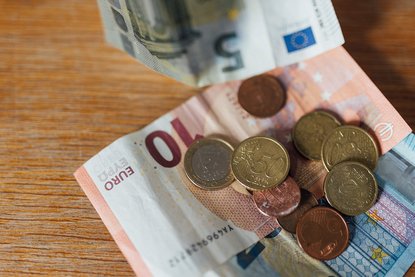 Euro-Geldscheine und Münzen liegen auf einem Holztisch