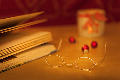 Buch und Brille mit Weihnachtskugeln im Hintergrund auf einem Tisch