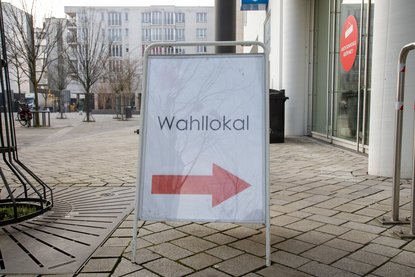 Wegweiser mit der Aufschrift Wahllokal und einem roten Pfeil nach rechts.