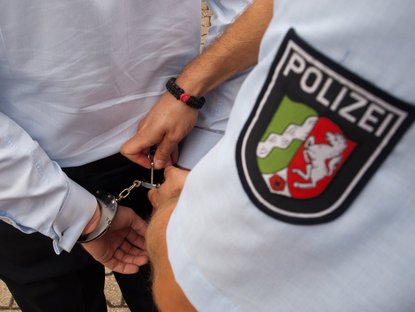 Polizist öffnet Handschellen an einer Person; Polizeilogo von NRW ist präsent im Bild