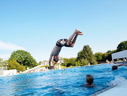 Mensch macht Köpper in ein Freibadbecken
