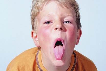 Junge in senfgelbem Shirt streckt die Zunge raus
