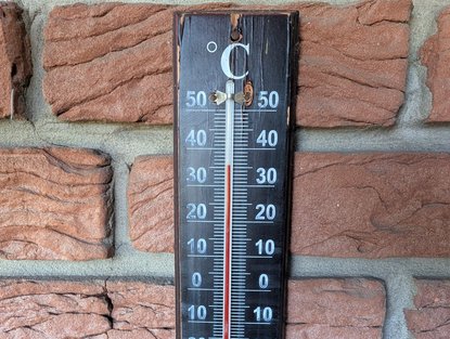 Braunes Thermometer an einer Hauswand zeigt 35 Grad.