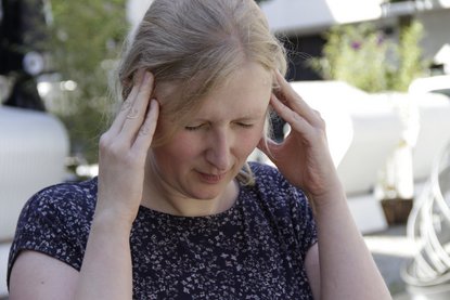 Frau hält sich mit schmerzverzogenem Gesicht die Schläfen